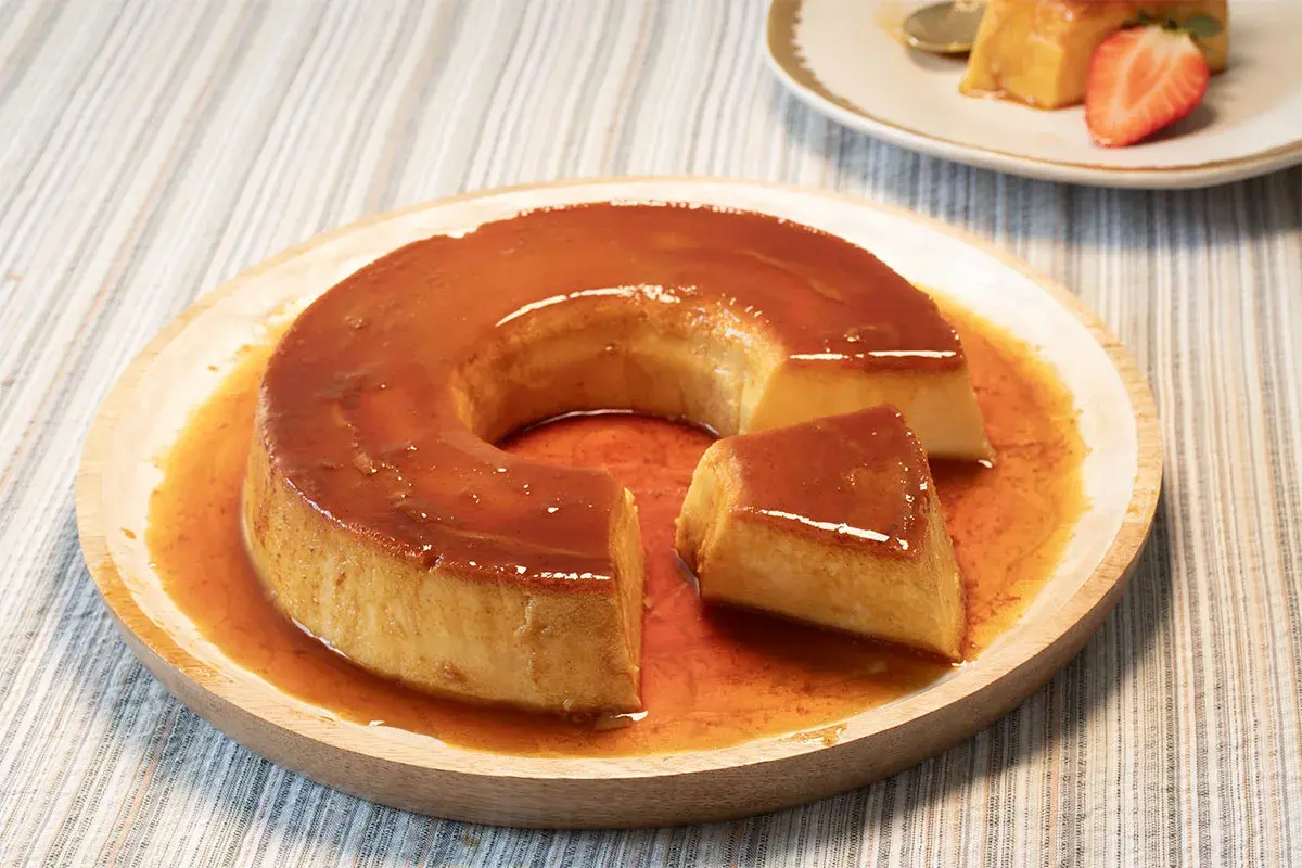 Un delicioso flan de leche condensada bañado en caramelo líquido, servido en un plato de madera.