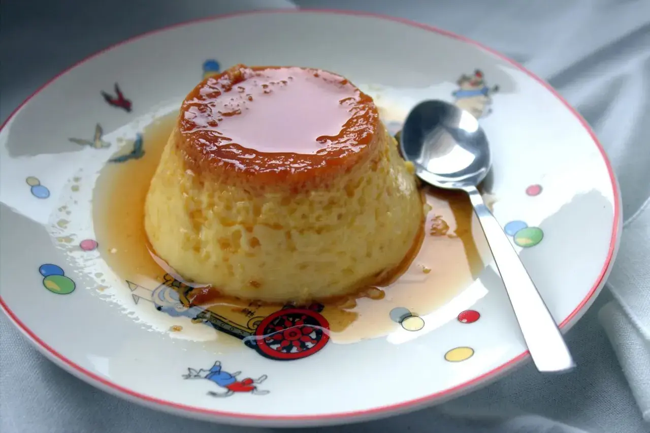 Delicioso flan de huevo casero con caramelo líquido, servido en un plato con dibujos infantiles.