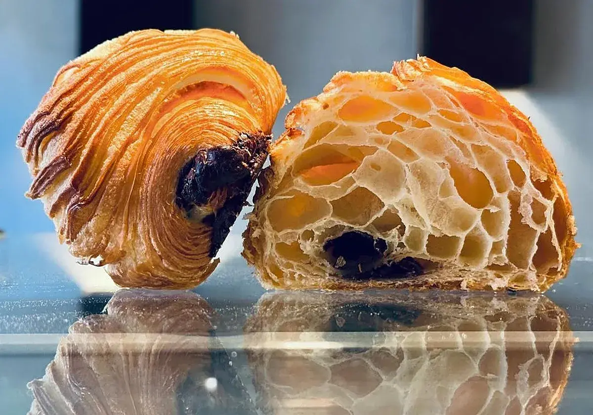 Dos mitades de un croissant de chocolate, una entera y otra cortada, revelan su interior aireado y el chocolate derretido.