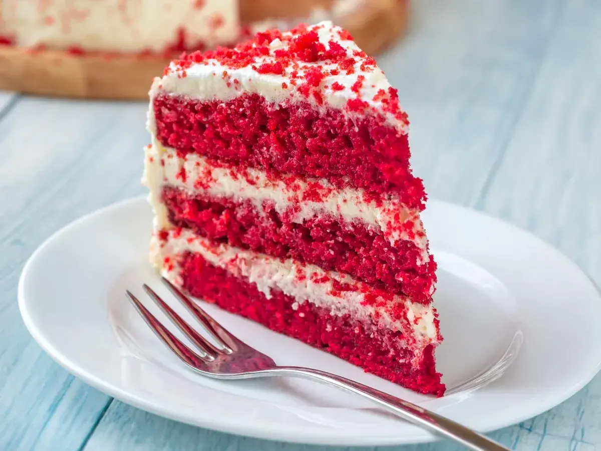 Rebanada de tarta red velvet con capas de bizcocho rojo y crema blanca, lista para disfrutar. Los ingredientes de esta tarta son un secreto delicioso.