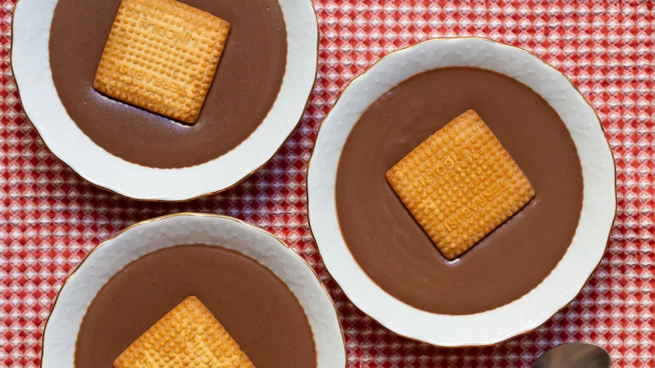 Tres cuencos de natillas de chocolate, cada uno con una galleta cuadrada encima, sobre un mantel de cuadros rojos y blancos.