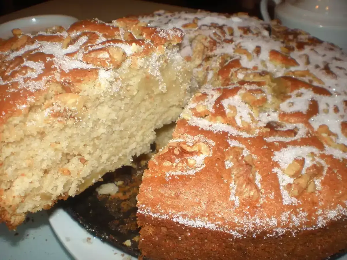Un delicioso bizcocho de manzana y nueces, espolvoreado con azúcar, con una rebanada retirada.
