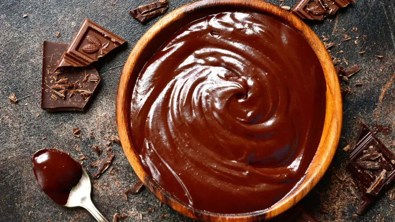 Un cuenco de madera lleno de cremoso de chocolate, con trozos de chocolate y virutas esparcidos alrededor.