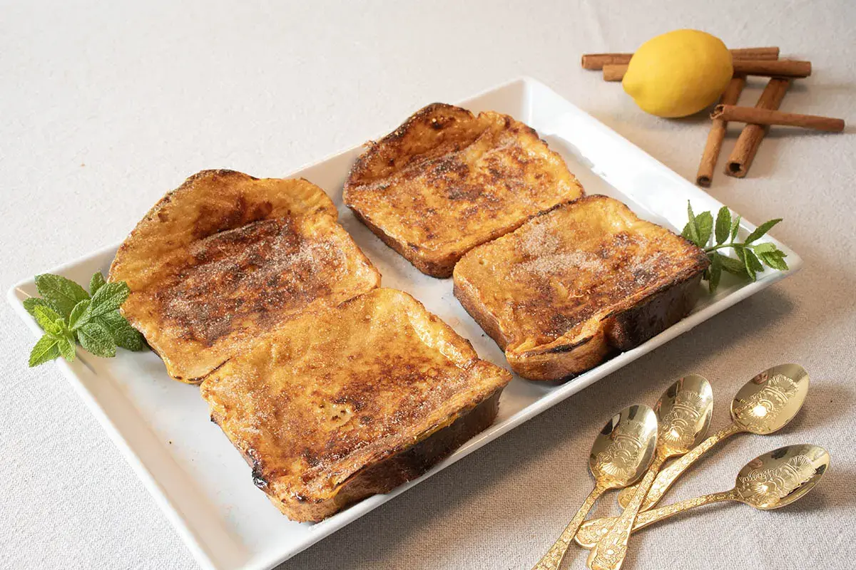 Cuatro deliciosas torrijas al horno, espolvoreadas con azúcar y canela, listas para disfrutar.