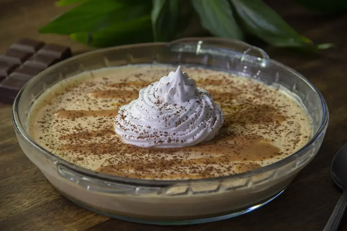 Delicioso mousse de dulce de leche en un bol de vidrio, coronado con crema batida y espolvoreado con cacao.