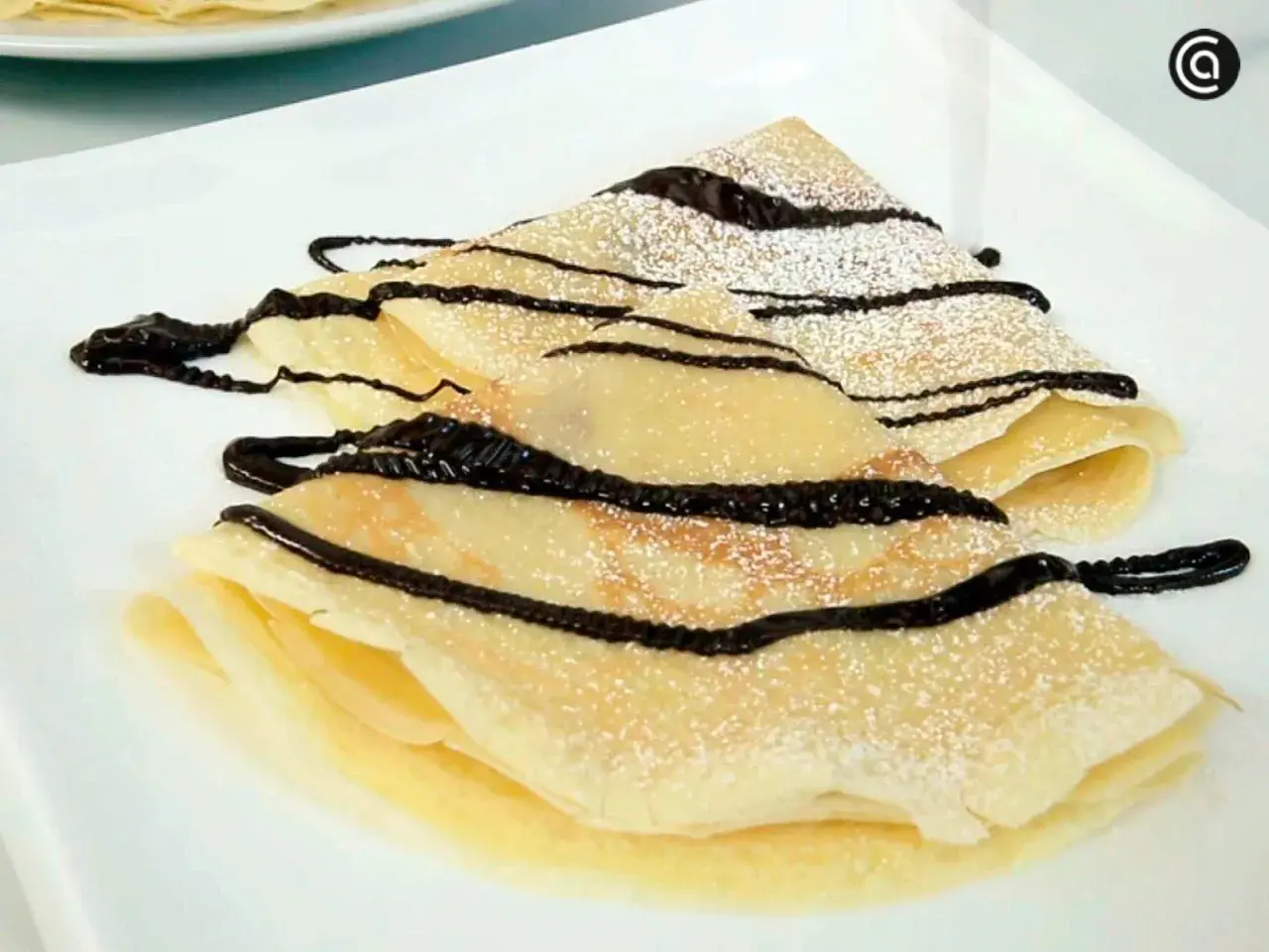Deliciosos crepes doblados, espolvoreados con azúcar glas y cubiertos con un glaseado de chocolate. Una receta crepes perfecta para cualquier ocasión.