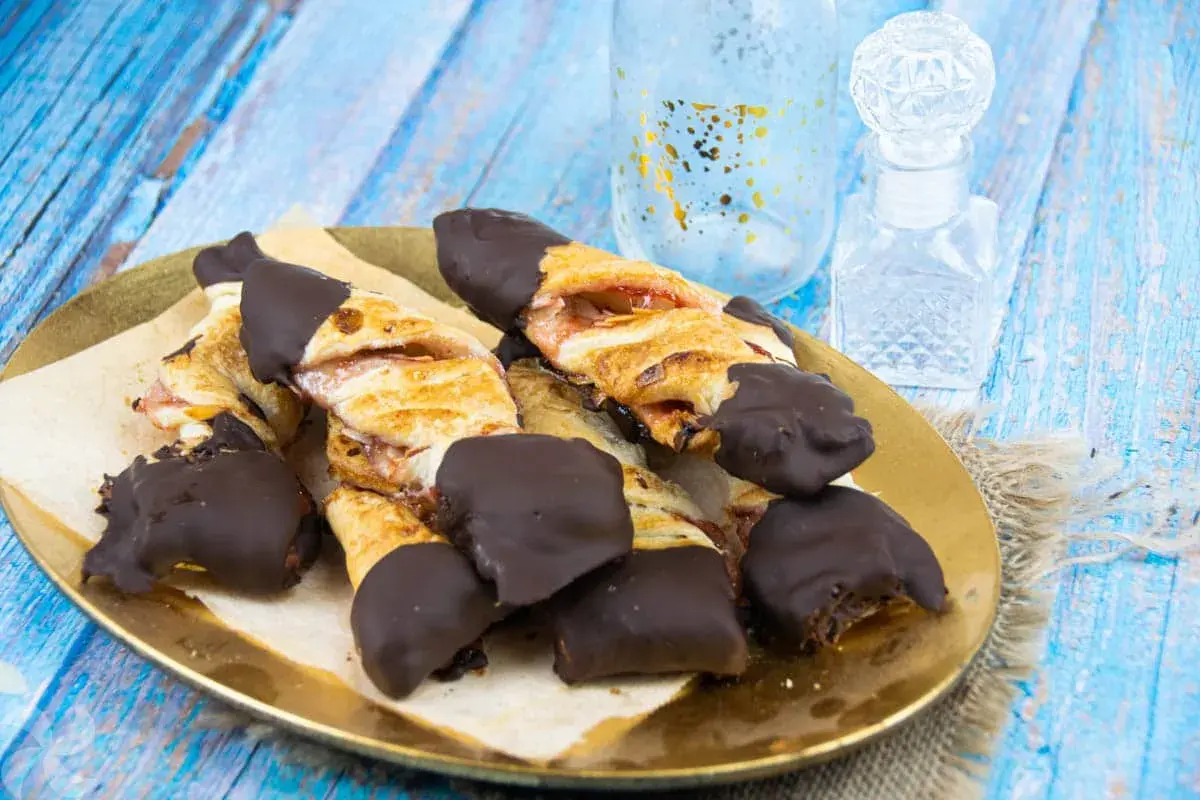 Deliciosos lazos de hojaldre con relleno de fresa, bañados en chocolate negro. Un dulce tentempié perfecto.