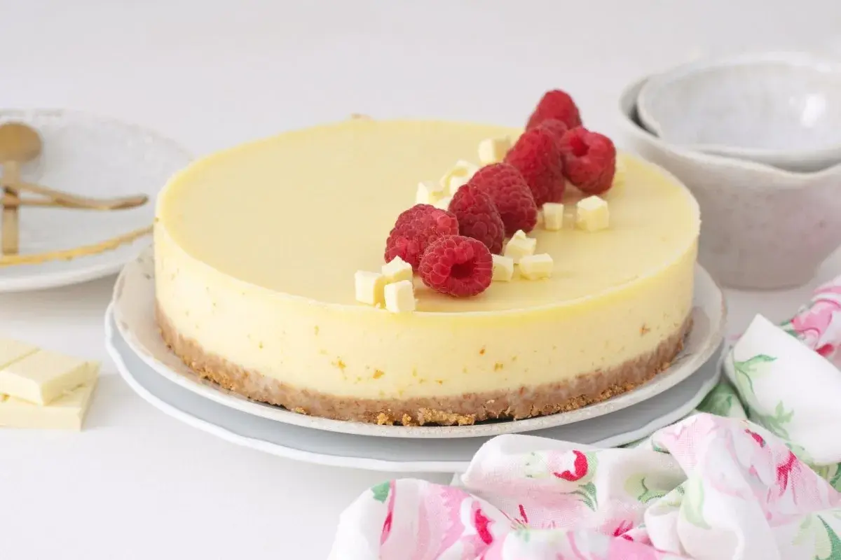 Deliciosa tarta de chocolate blanco adornada con frambuesas frescas y trocitos de chocolate.