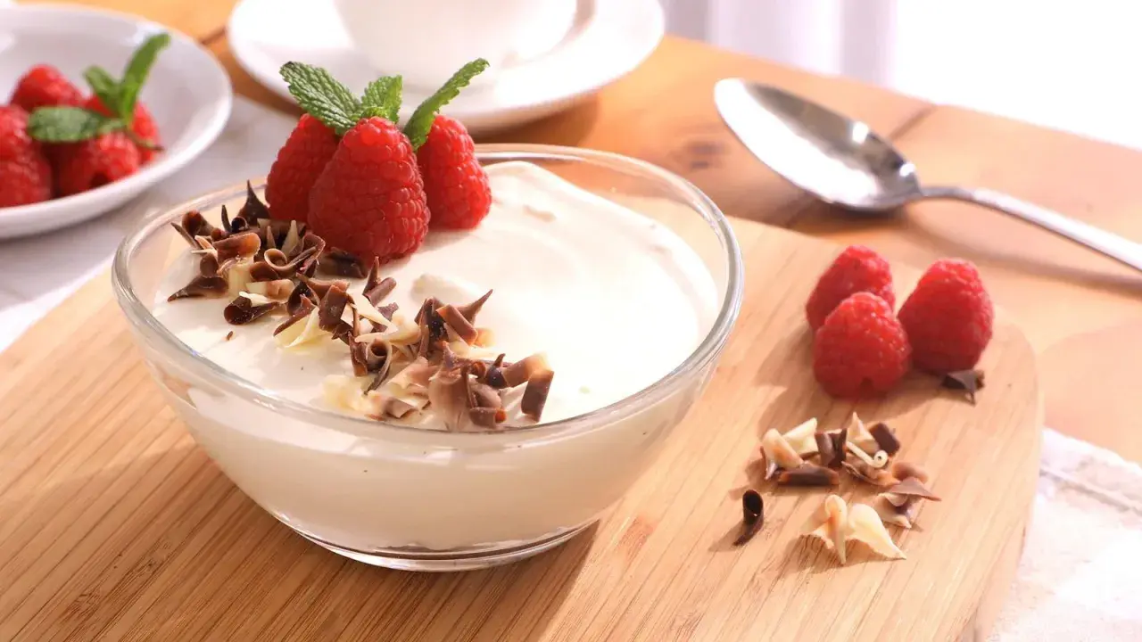 Delicioso mousse de chocolate blanco adornado con frambuesas frescas y virutas de chocolate.