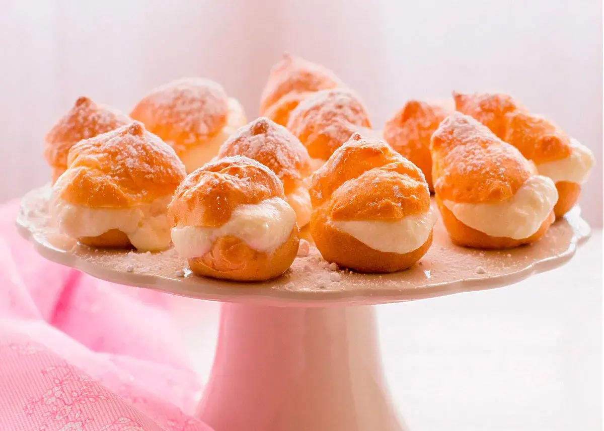 Deliciosos profiteroles de nata, espolvoreados con azúcar glas, listos para ser disfrutados en una bandeja blanca.