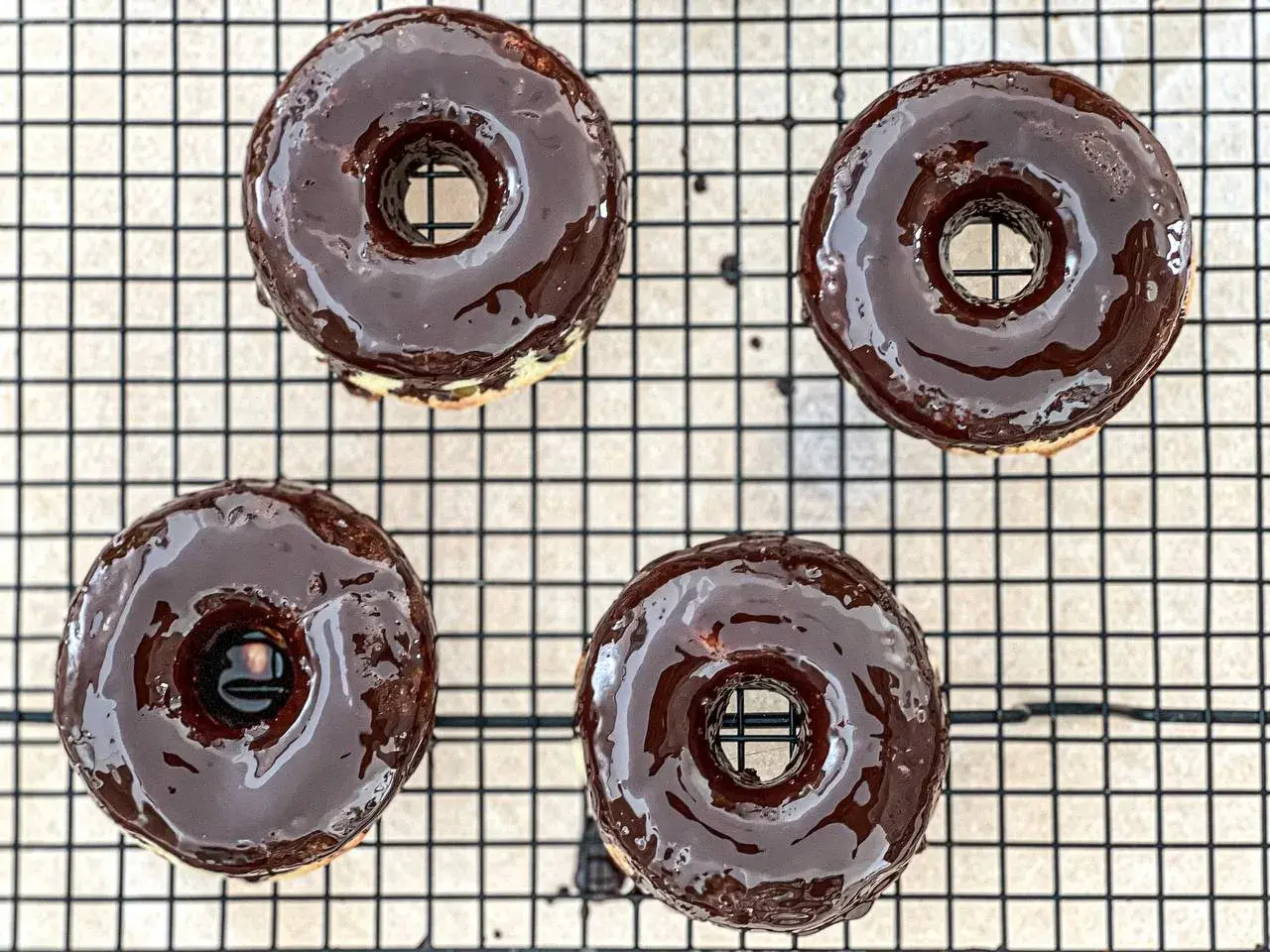 Cuatro deliciosos donuts glaseados con chocolate oscuro, listos para disfrutar. ¡Así es como hacer donuts caseros!