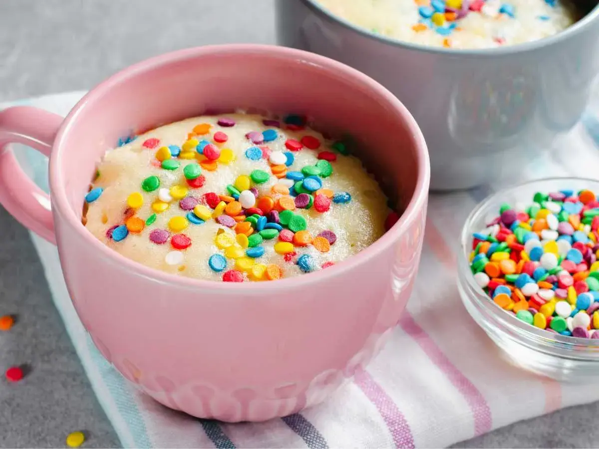 Un delicioso bizcocho al microondas en una taza rosa, cubierto de coloridas chispas. ¡Listo para disfrutar en minutos!