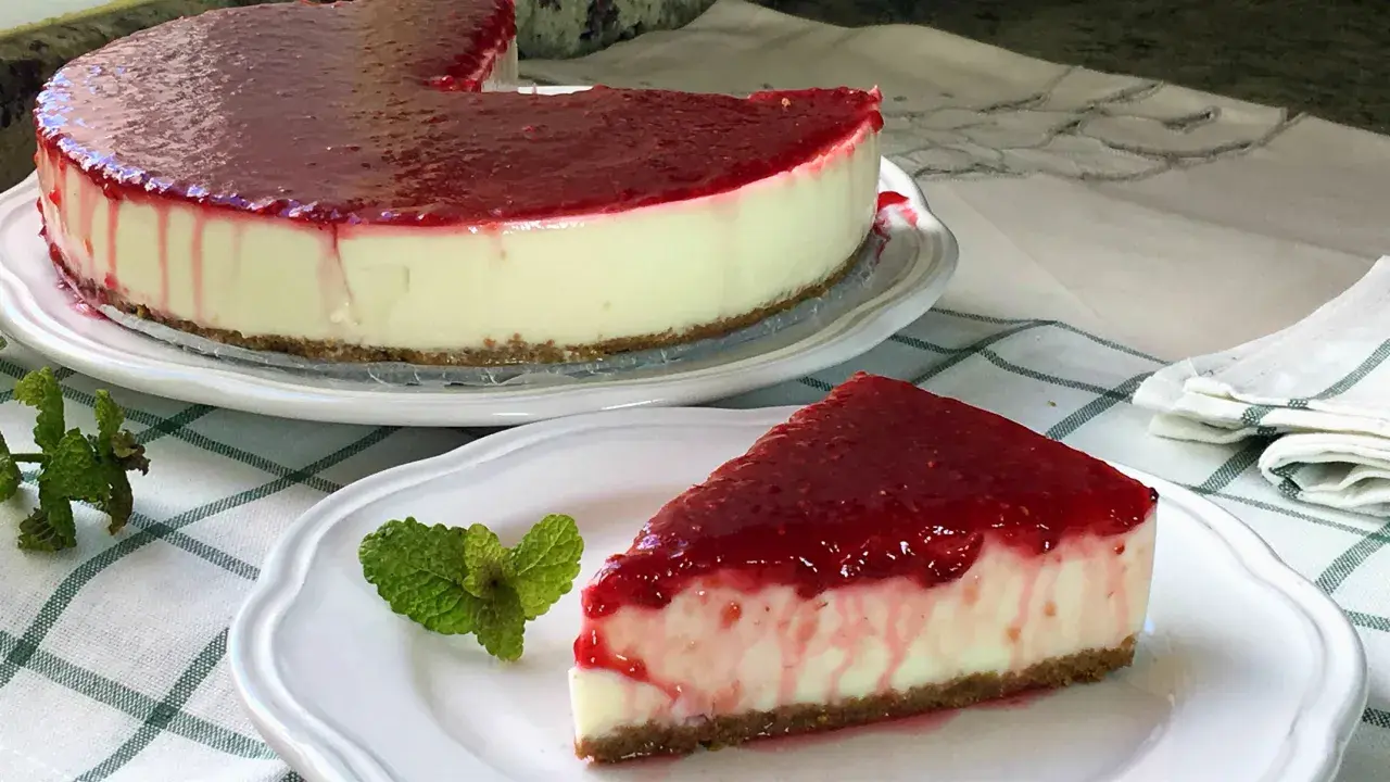 Deliciosa tarta de yogur sin horno cubierta con mermelada de frutos rojos. Un trozo servido con menta fresca.