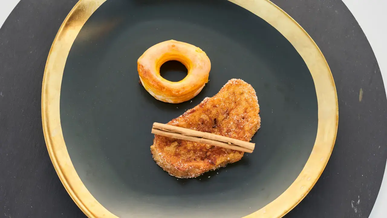 Rosquillas de Alcalá y torrija con canela, servidas en plato negro con borde dorado.