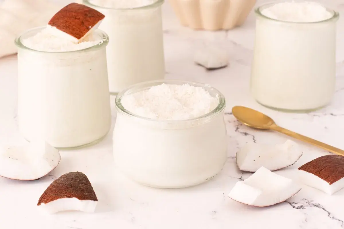 Delicioso mousse de coco en vasitos de cristal, decorado con coco rallado y trozos de coco fresco.