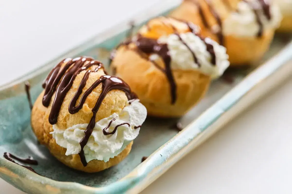 Profiteroles rellenos de crema y bañados en chocolate, perfectos para tu próxima receta.