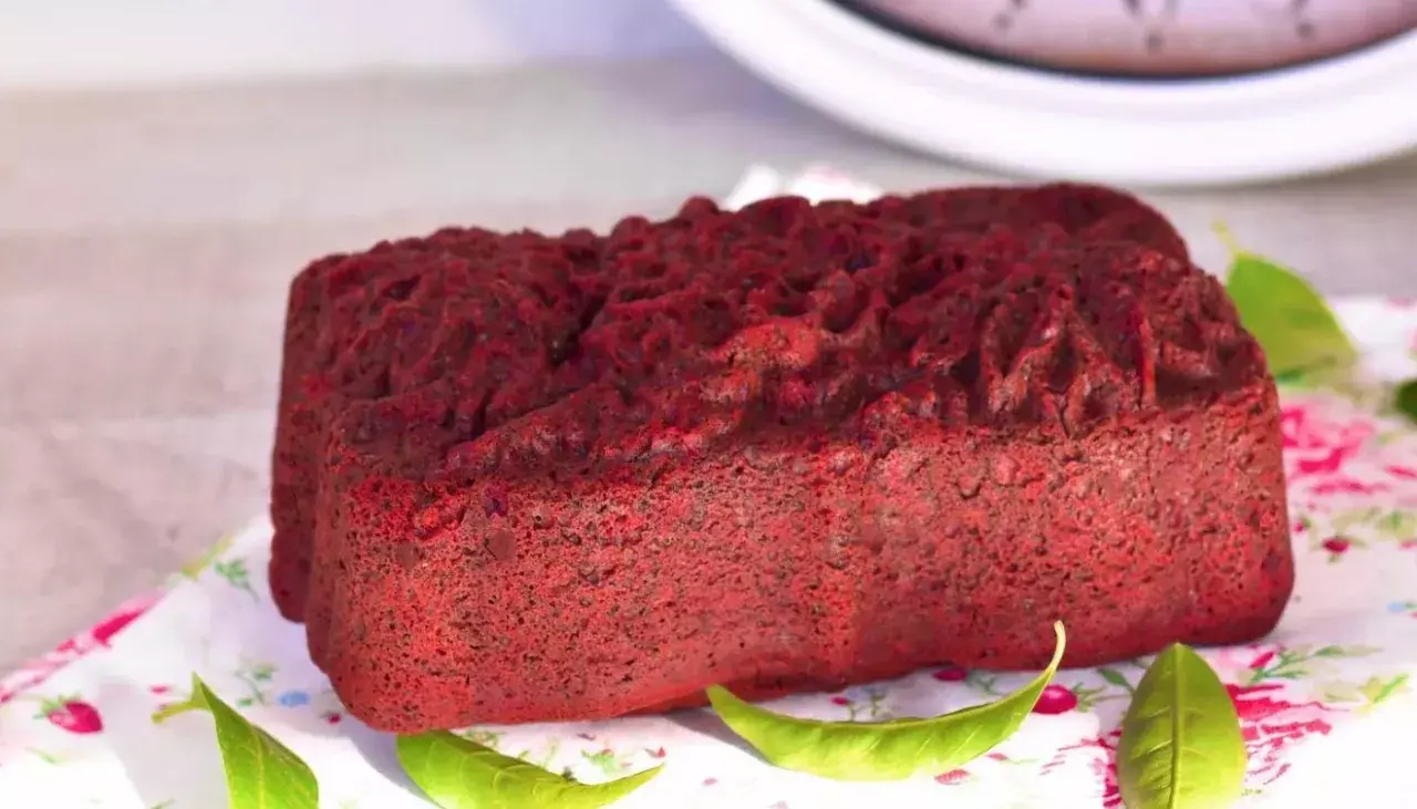 Un delicioso pan de red velvet, con una textura esponjosa y un color vibrante, decorado con hojas verdes sobre un mantel floral.