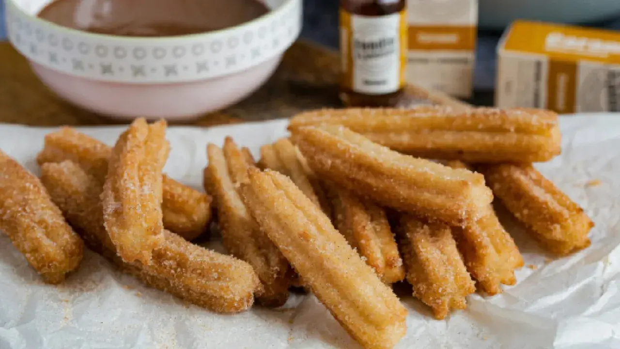 Montón de churros caseros recién hechos, espolvoreados con azúcar y canela, listos para mojar en chocolate caliente.