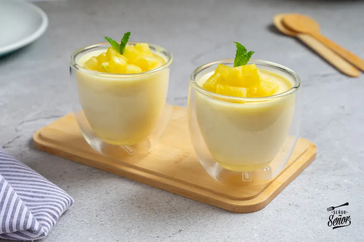 Dos copas de cristal con un delicioso mousse de piña, decoradas con trocitos de piña y menta.