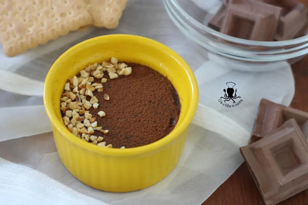 Pudín de chocolate cremoso en un cuenco amarillo, espolvoreado con cacao y nueces picadas.