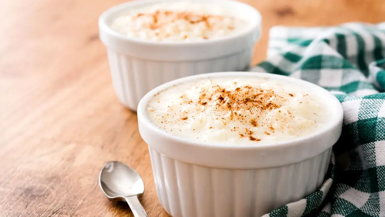Dos ramequines de arroz con leche en microondas, espolvoreados con canela, sobre una mesa de madera.