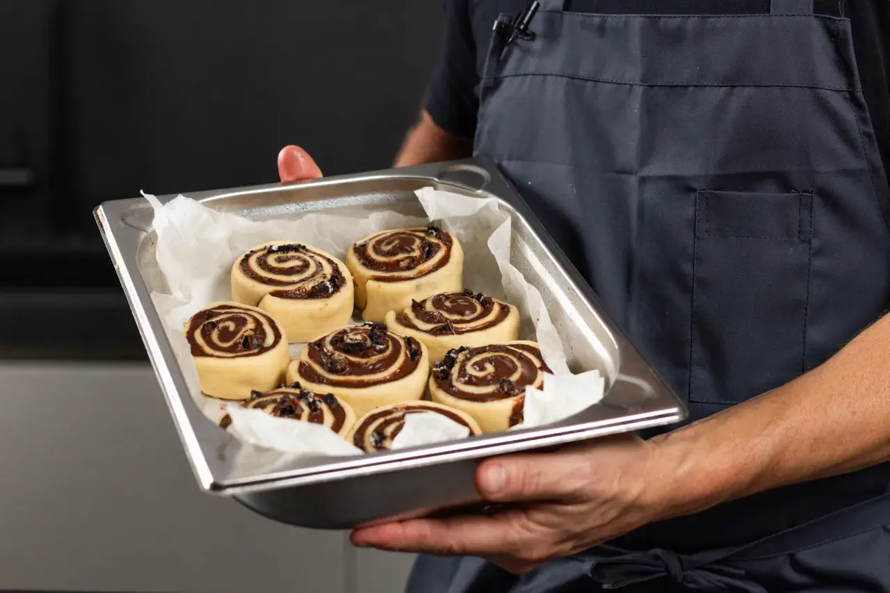 Manos sostienen una bandeja con deliciosos rollitos de canela listos para hornear.