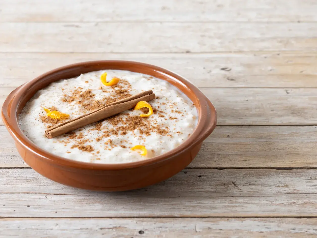 Un tazón de arroz con leche cremoso, espolvoreado con canela y adornado con cáscara de naranja y una rama de canela. ¡Perfecto para tu receta de arroz con leche cremoso!