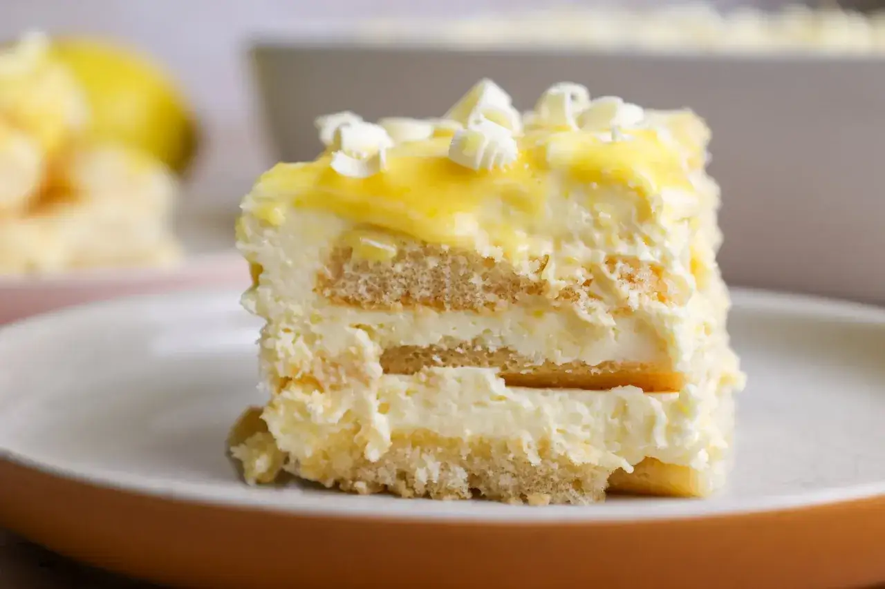 Rebanada de tiramis&uacute; de lim&oacute;n, con capas de bizcocho y crema, cubierta de glaseado amarillo y virutas de chocolate blanco.