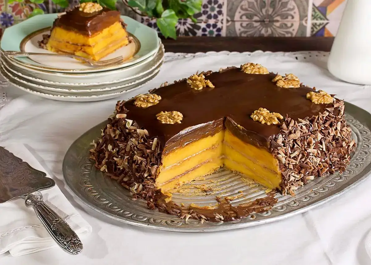 La tarta de la abuela, con capas de crema y bizcocho, cubierta de chocolate y nueces, lista para ser servida.
