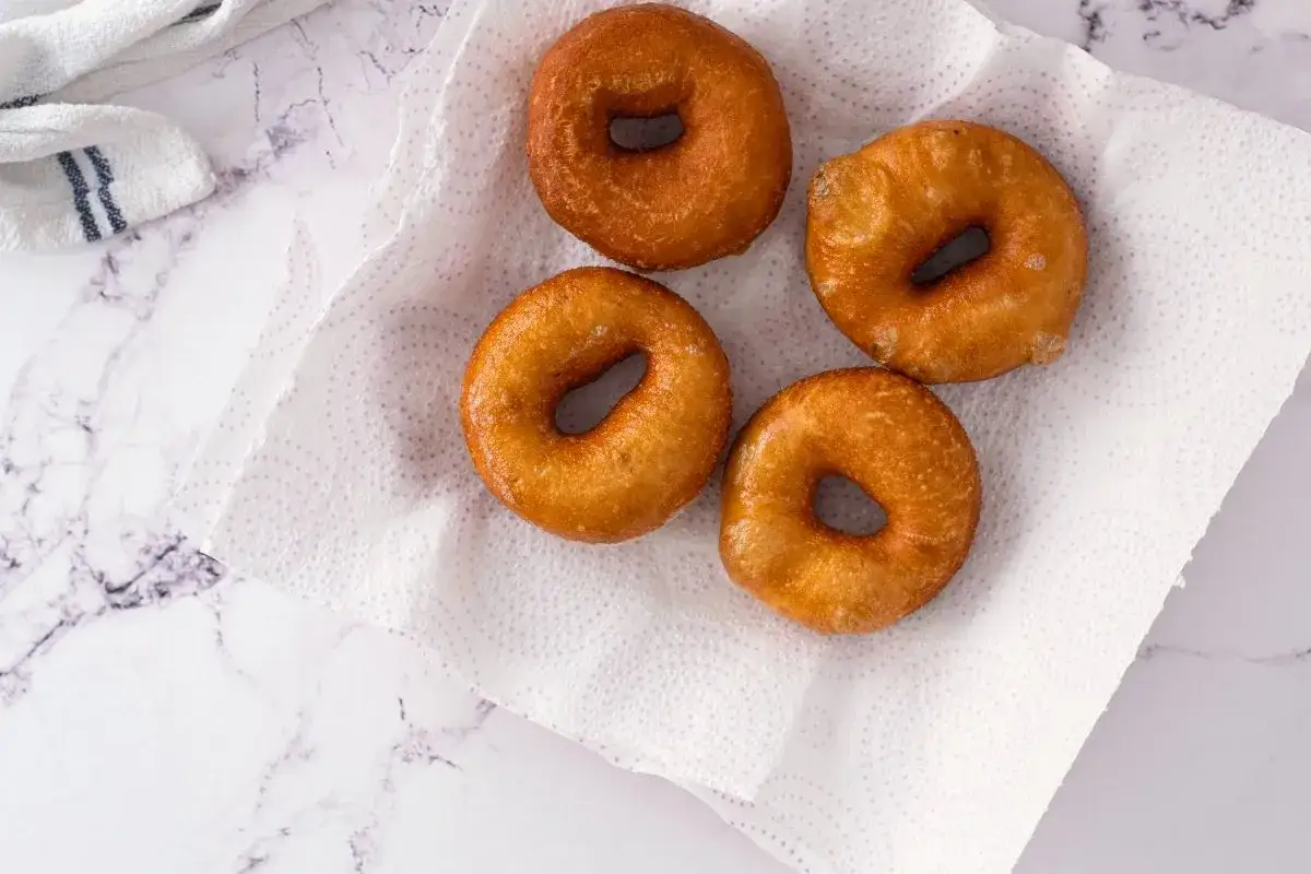 Cuatro roscos fritos dorados sobre papel absorbente, listos para disfrutar. Una deliciosa receta de roscos fritos caseros.