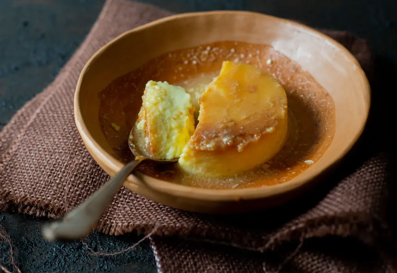 Un trozo de flan de yogur cremoso en un cuenco de barro, con una cuchara lista para probarlo.
