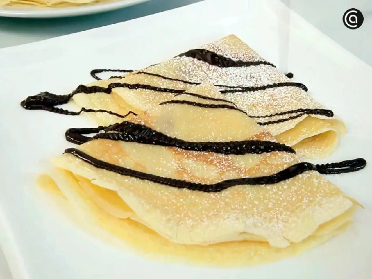 Deliciosos crepes doblados, espolvoreados con az&uacute;car glas y cubiertos con sirope de chocolate. Una receta f&aacute;cil y r&aacute;pida.