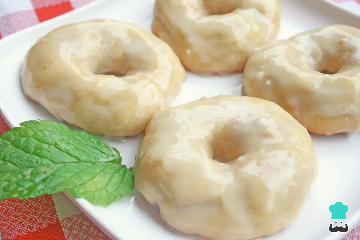 Cuatro deliciosos donuts al horno con glaseado blanco, servidos en un plato blanco junto a una hoja de menta fresca.