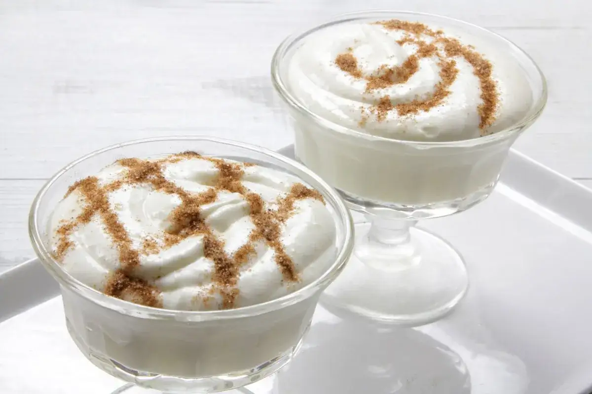Dos copas de mousse de arroz con leche, adornadas con canela espolvoreada, listas para disfrutar.