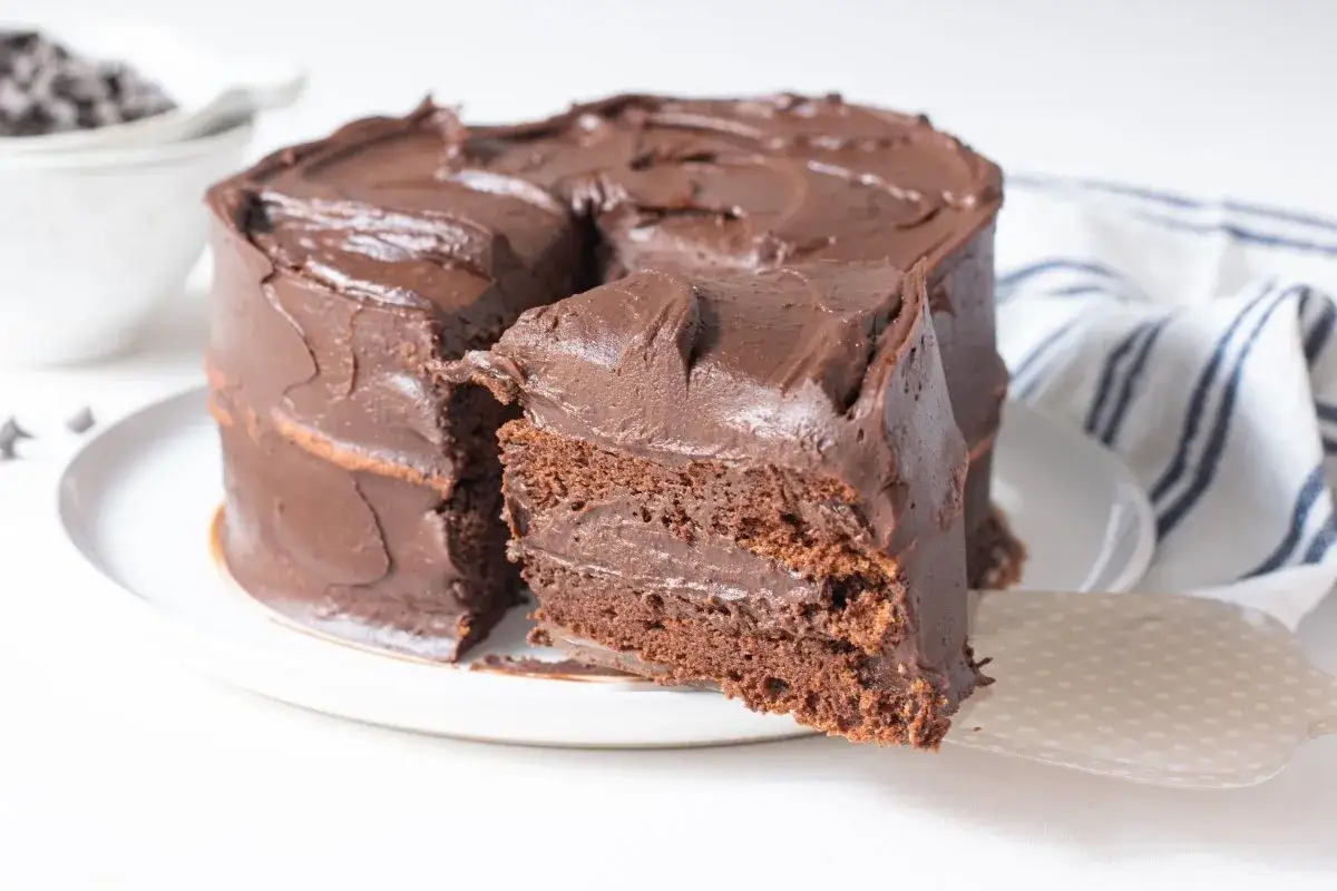 Una deliciosa tarta de chocolate, cubierta con glaseado cremoso y una rebanada lista para servir.