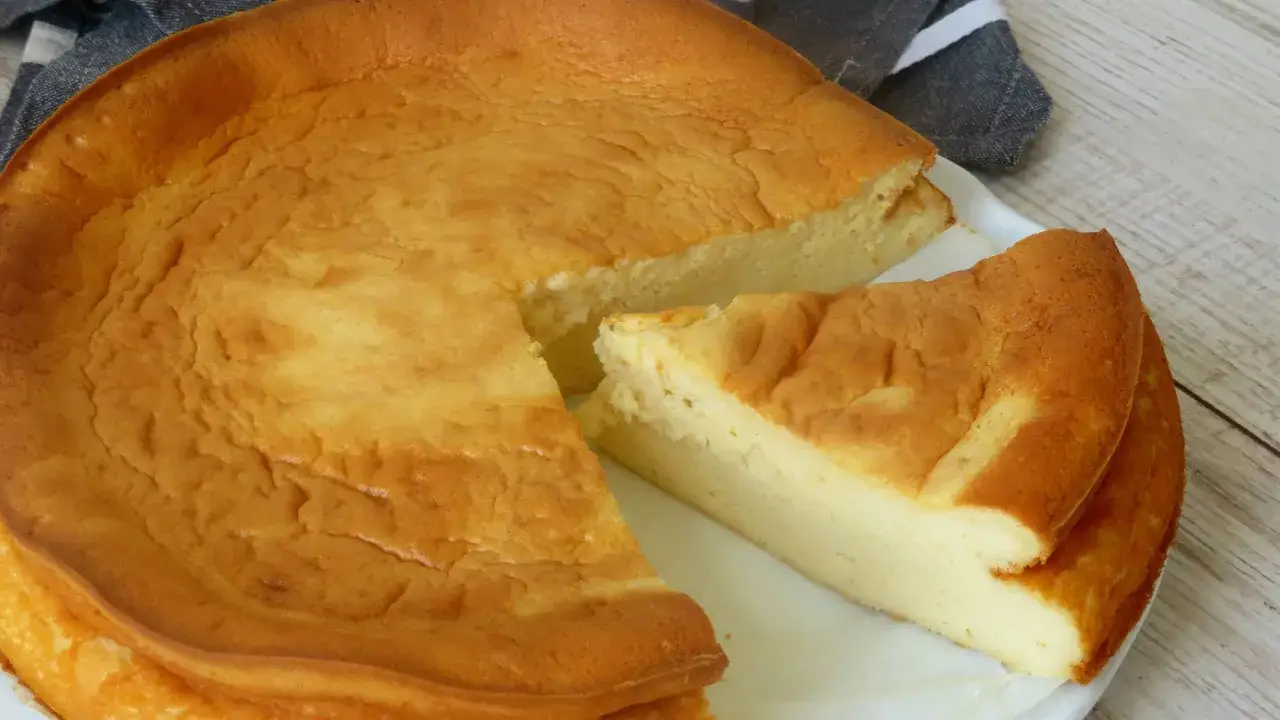 Tarta de queso Philadelphia reci&eacute;n horneada, con una rebanada separada que muestra su interior cremoso y dorado.
