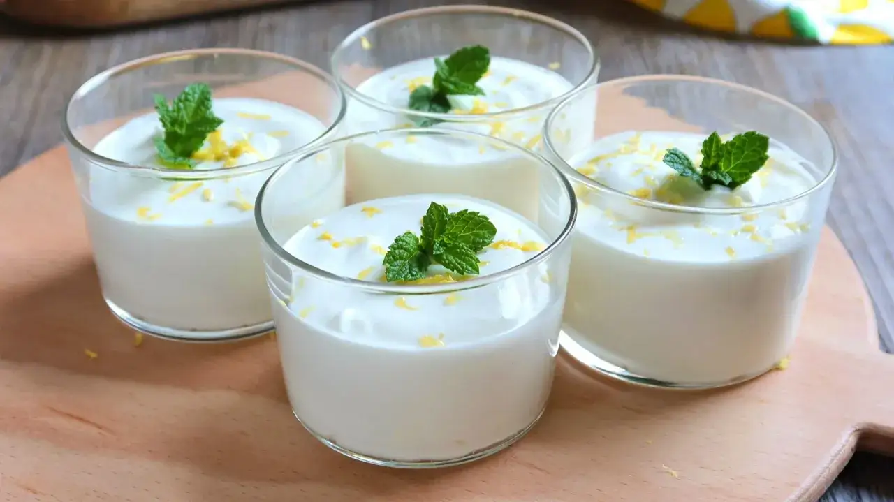 Cuatro vasitos de mousse de lim&oacute;n, decorados con ralladura de lim&oacute;n y hojas de menta fresca, listos para disfrutar.