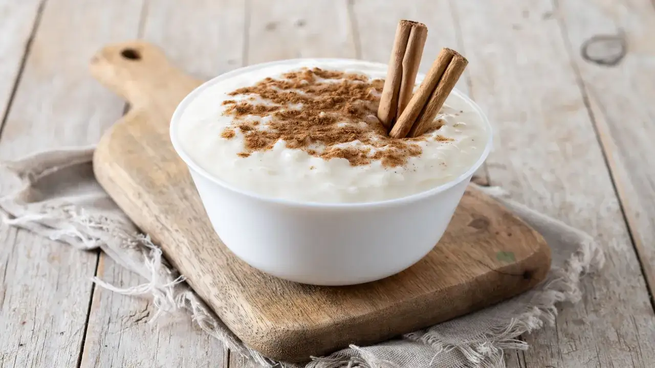 Delicioso arroz con leche thermomix, cremoso y espolvoreado con canela y dos ramas de canela.