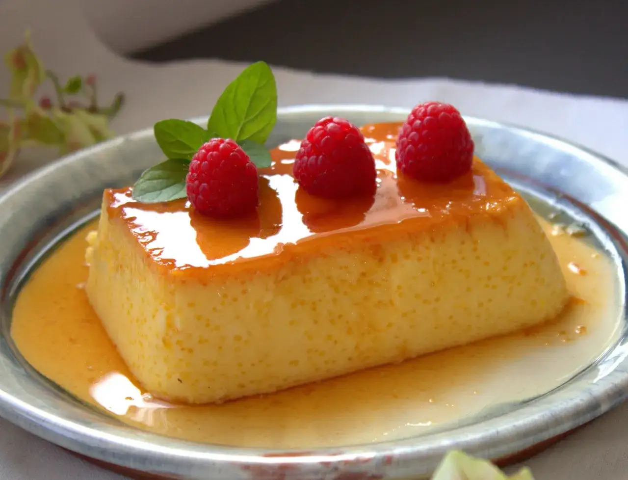 Delicioso flan de queso sin horno, cubierto con caramelo líquido y adornado con frambuesas y menta fresca.