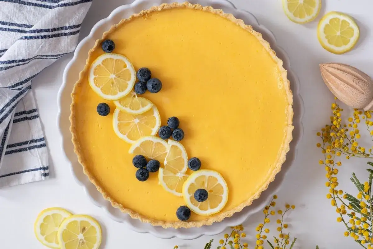 Tarta de lim&oacute;n con leche condensada, decorada con rodajas de lim&oacute;n y ar&aacute;ndanos. Un postre refrescante y delicioso.