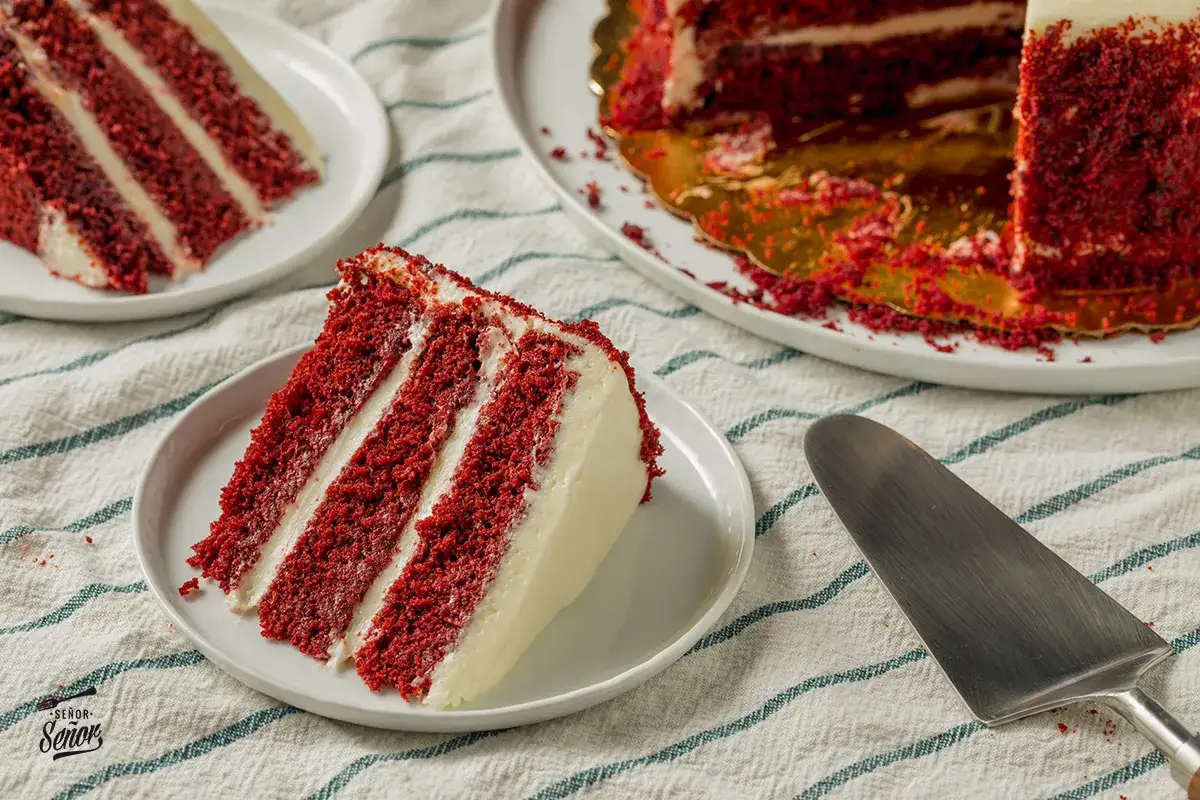 Porci&oacute;n de tarta red velvet con capas de bizcocho rojo y crema blanca. Los ingredientes para esta delicia se intuyen en la imagen.