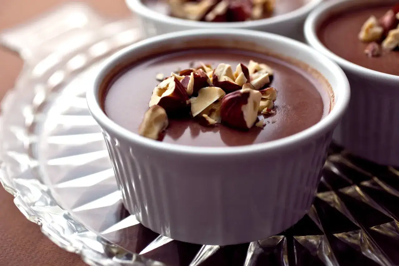 Deliciosa panna cotta de Nutella, cremosa y cubierta con trozos de avellanas tostadas, servida en ramequines blancos sobre una bandeja de cristal.