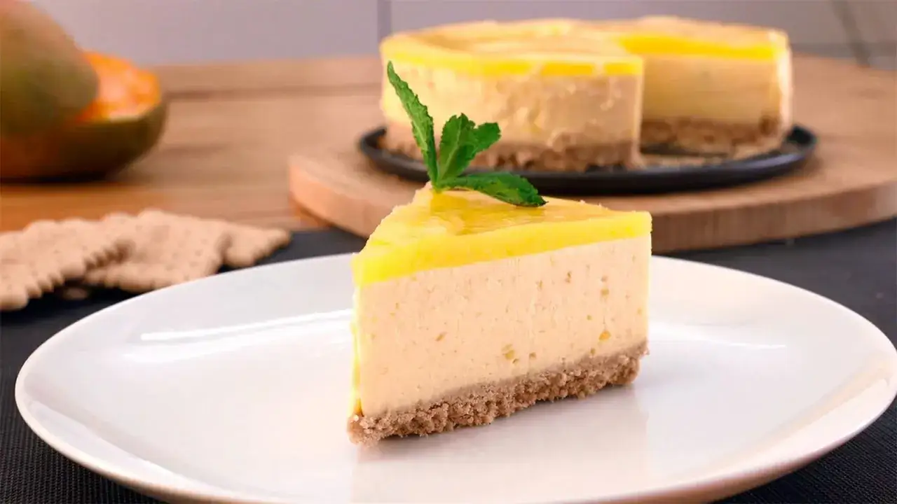 Rebanada de tarta de mango y queso con cobertura amarilla brillante y hoja de menta.
