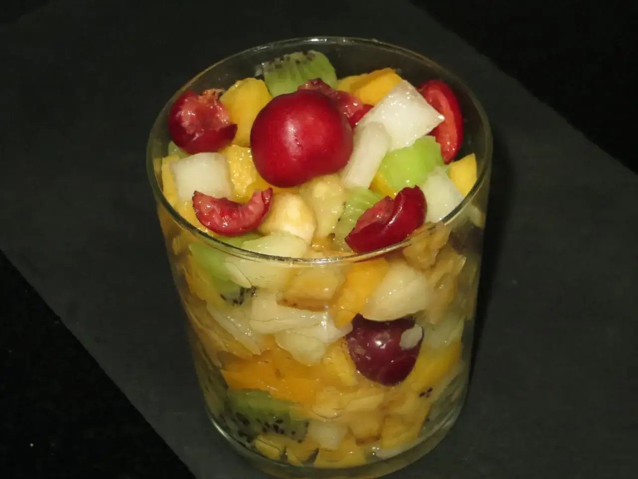 Deliciosa macedonia de frutas en vaso: kiwi, mango, mel&oacute;n y cerezas. Un postre refrescante y lleno de color.