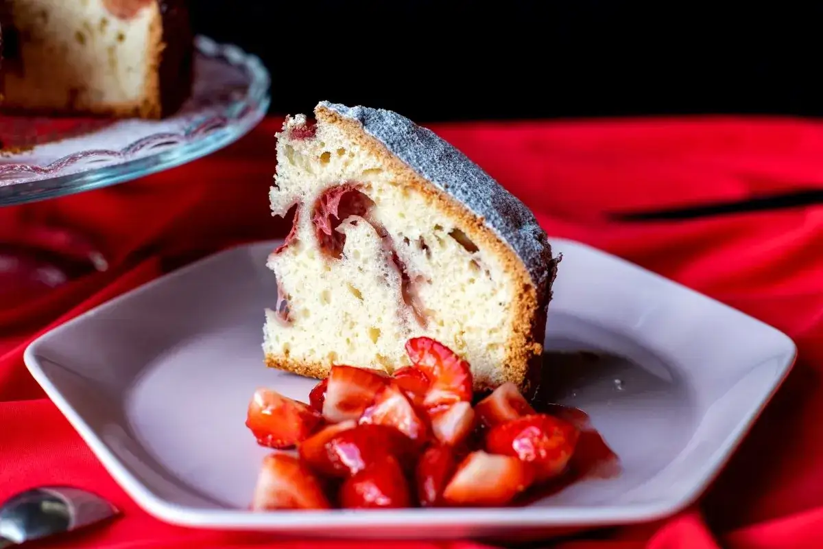 Rebanada de bizcocho de fresa esponjoso con trozos de fresa y az&uacute;car glas, servido con fresas picadas.