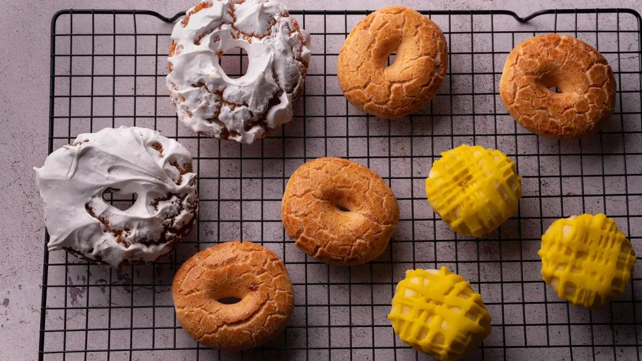 Rosquillas de San Isidro: dos cubiertas de merengue blanco y varias doradas con textura crujiente, junto a otras ba&ntilde;adas en glaseado amarillo.