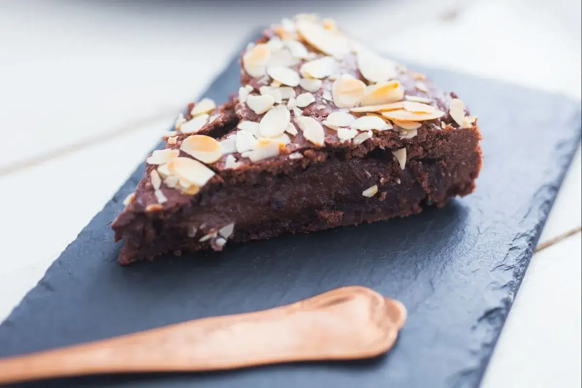 Deliciosa tarta del abuelo de chocolate, cubierta con almendras laminadas, servida en pizarra con una cuchara de cobre.