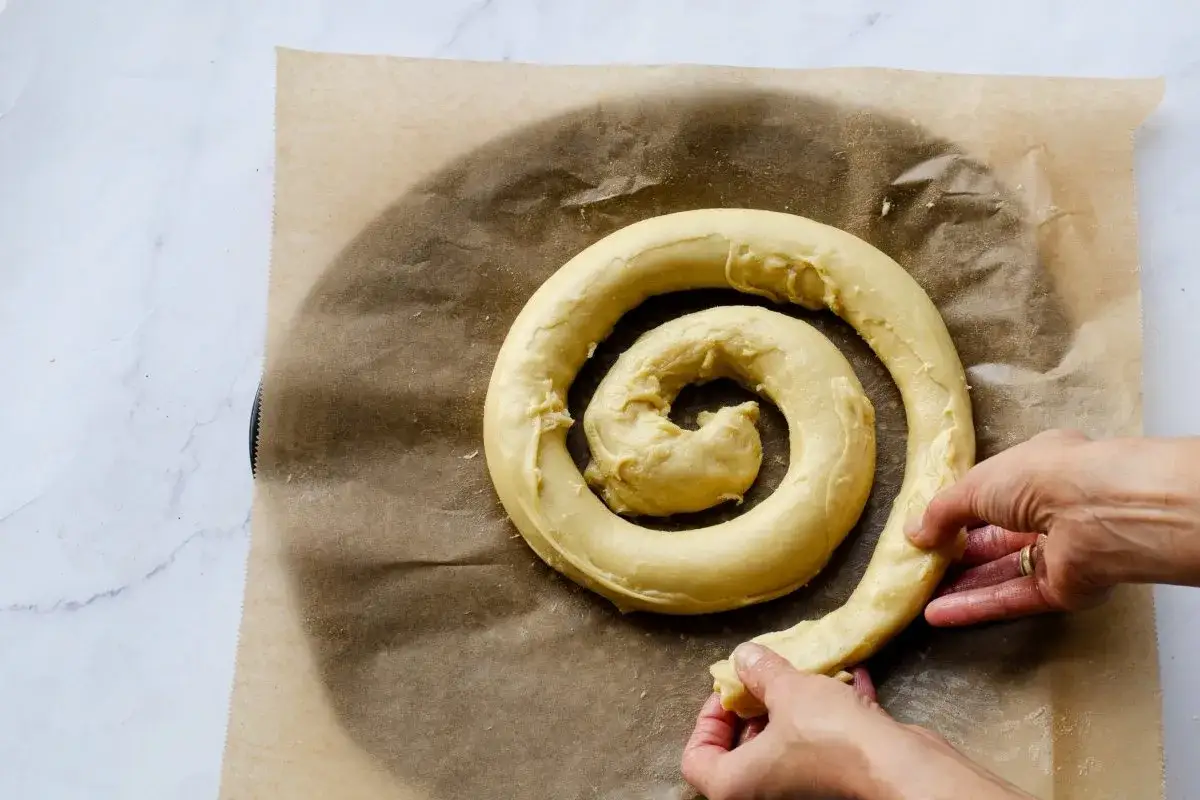 Manos dan forma a una ensaimada mallorquina cruda, enrollada en espiral sobre papel de horno.