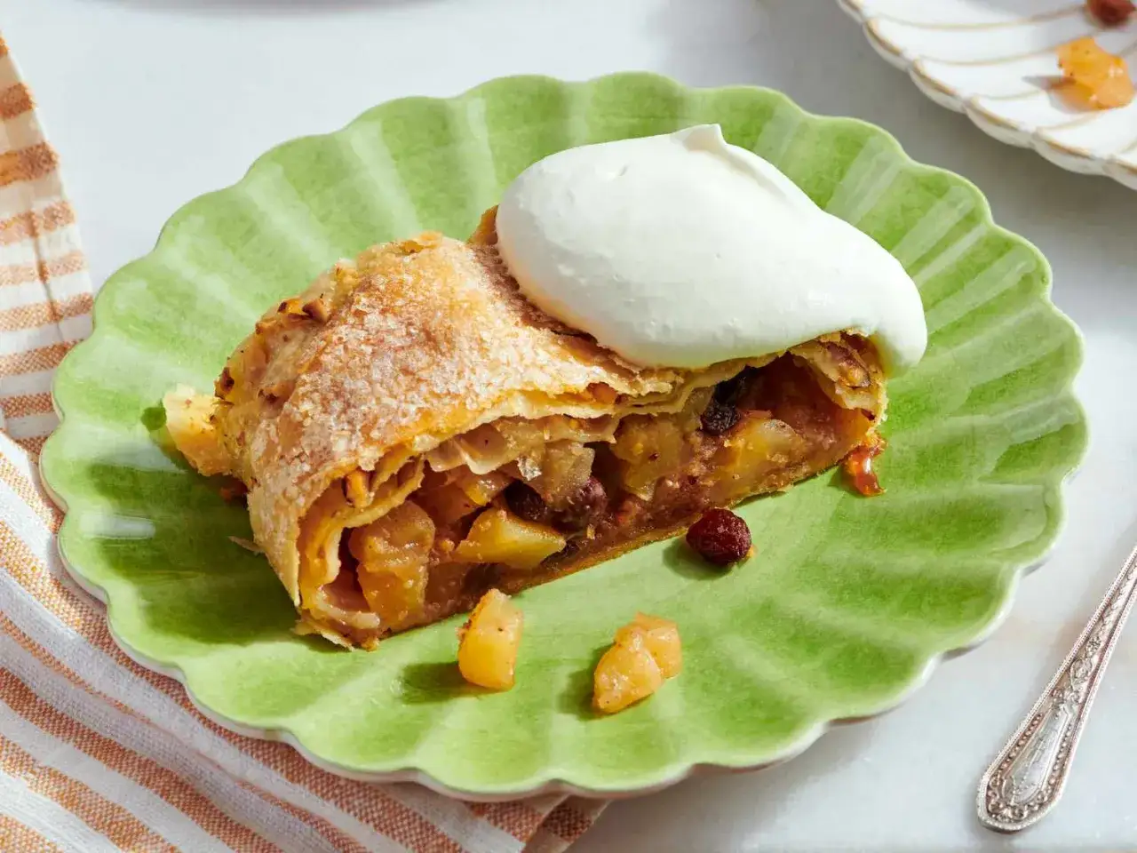 Un trozo de strudel de manzana, con su masa dorada y relleno de fruta, coronado con una generosa porci&oacute;n de nata montada.