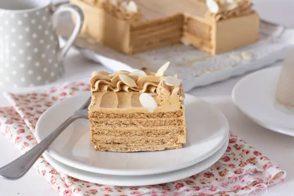 Deliciosa tarta de moka en capas, decorada con crema y almendras. Un trozo servido en plato blanco, listo para disfrutar.